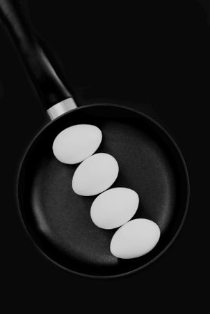 four white raw eggs in the shell lie on a black frying pan standing on a black background ready for breakfastの写真素材