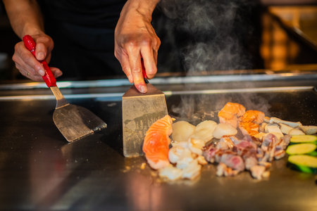chef's hands with spatula over teppanyaki. cooking vegetables meat and seafood on hot hibachi grill table. Traditional Japanese Cuisine. Teppan showの写真素材