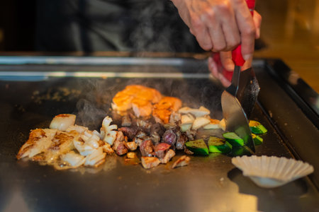 chef's hands with spatula over teppanyaki. cooking vegetables meat and seafood on hot hibachi grill table. Traditional Japanese Cuisine. Teppan showの写真素材