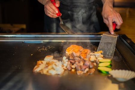 chef's hands with spatula over teppanyaki. cooking vegetables meat and seafood on hot hibachi grill table. Traditional Japanese Cuisine. Teppan showの写真素材