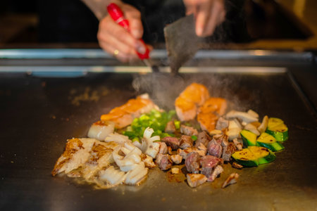 chef's hands with spatula over teppanyaki. cooking vegetables meat and seafood on hot hibachi grill table. Traditional Japanese Cuisine. Teppan showの写真素材