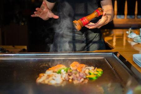chef's hands with spatula over teppanyaki. cooking vegetables meat and seafood on hot hibachi grill table. Traditional Japanese Cuisine. Teppan showの写真素材