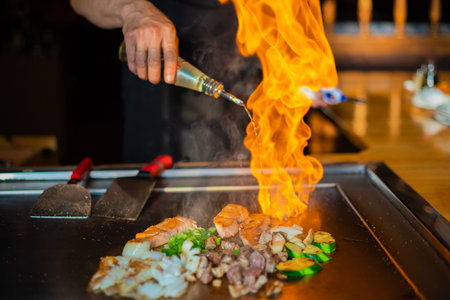 chef's hands with spatula over teppanyaki. cooking vegetables meat and seafood on hot hibachi grill table. Traditional Japanese Cuisine. Teppan show with flameの写真素材