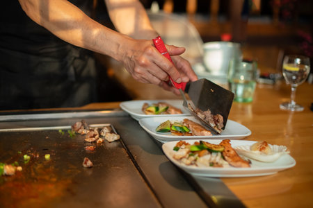 chef's hands with spatula over teppanyaki. cooking vegetables meat and seafood on hot hibachi grill table. Traditional Japanese Cuisine. Teppan showの写真素材