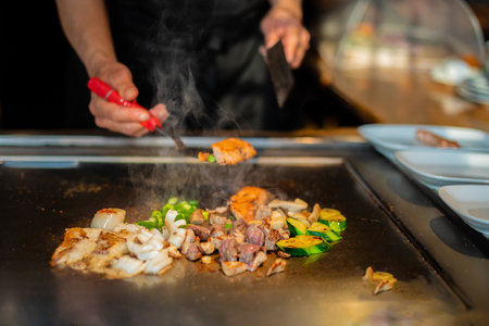 chef's hands with spatula over teppanyaki. cooking vegetables meat and seafood on hot hibachi grill table. Traditional Japanese Cuisine. Teppan showの写真素材