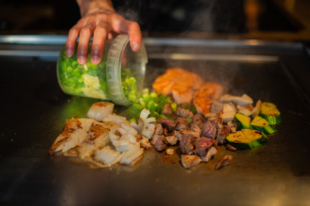 chef's hands with spatula over teppanyaki. cooking vegetables meat and seafood on hot hibachi grill table. Traditional Japanese Cuisine. Teppan showの写真素材