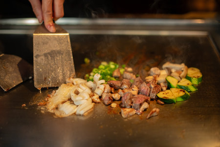 chef's hands with spatula over teppanyaki. cooking vegetables meat and seafood on hot hibachi grill table. Traditional Japanese Cuisine. Teppan showの写真素材