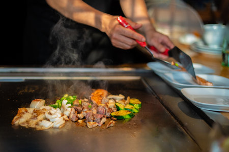chef's hands with spatula over teppanyaki. cooking vegetables meat and seafood on hot hibachi grill table. Traditional Japanese Cuisine. Teppan showの写真素材