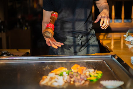 chef's hands with spatula over teppanyaki. cooking vegetables meat and seafood on hot hibachi grill table. Traditional Japanese Cuisine. Teppan showの写真素材