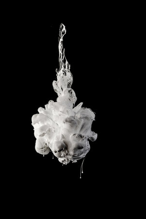 Ink dropped in water and photographed while in motion. Paint swirling. Gray and white cloud and smoke of paint isolated on black background.の写真素材
