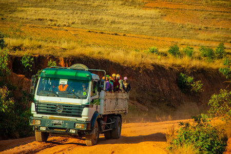 Madagascar, 10. 22. 2023. group of Malagasy people rides in back of truck while standing on a clayey, dusty yellow road on hot sunny dayの写真素材
