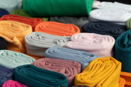 Rolled fabric textiles in various colors are neatly arranged, showing textures and patterns for creative design projects.の写真素材