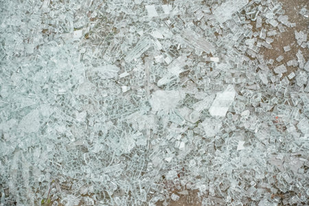 Broken glass fragments are spread across the ground, showcasing sharp edges and a reflective quality, creating a striking visual scene.の写真素材