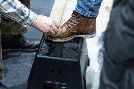 Individual is polishing a brown leather boot while standing on a black stool, showing attention to...