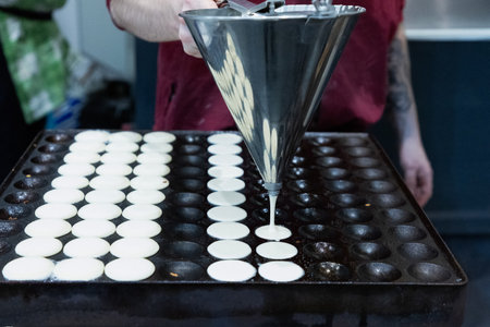 Culinary expert is pouring batter into a large cooking surface, creating perfectly round pancakes in...