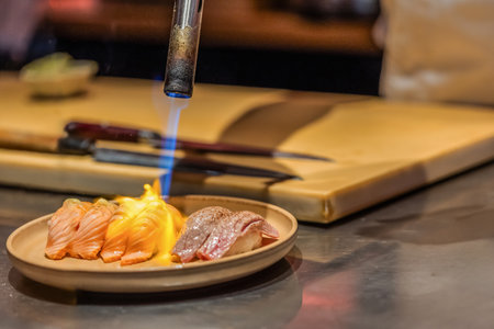 Culinary artist is using a torch to sear sushi on a plate in a modern kitchen, showcasing vibrant colors and intricate food presentation.の写真素材