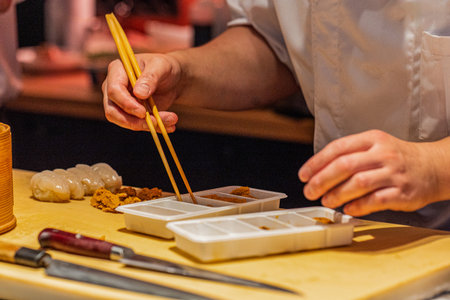 Chef is skillfully preparing sushi using chopsticks on a wooden countertop, showing culinary expertise and attention to detail.の写真素材