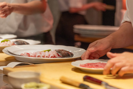 Chef is preparing sushi on a wooden counter, showcasing fresh ingredients and meticulous attention to detail in a vibrant kitchen environment.の写真素材