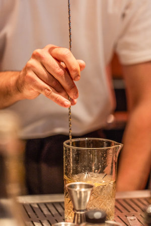 Bartender is mixing a cocktail in a glass using a stirring tool, surrounded by various bar equipment...