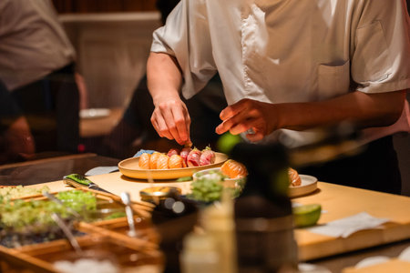 Sushi chef skillfully prepares fresh sushi rolls, showcasing vibrant ingredients and meticulous technique in a lively culinary environment.の写真素材