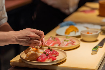 Sushi chef is carefully arranging a vibrant sushi platter with fresh ingredients, showcasing culinary artistry and attention to detail.の写真素材