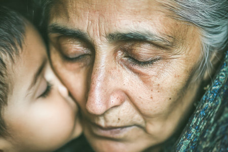 . Elderly woman is embracing a child who is kissing her cheek, showcasing a warm and intimate moment filled with love and connectionの素材