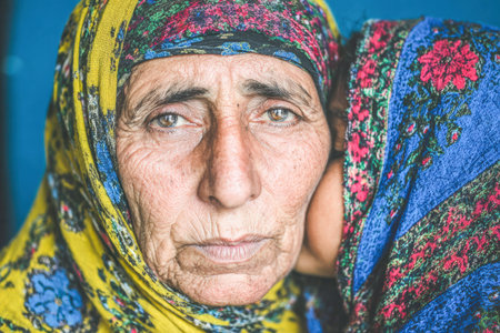 . Elderly woman with a vibrant headscarf is embracing a young girl, showcasing warmth and affection in a close-up portrait with rich texturesの素材