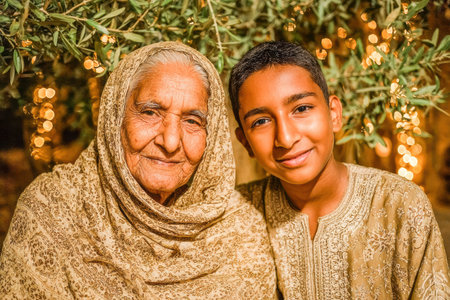 . Elderly woman and young boy are smiling together in a warm outdoor setting, surrounded by soft lights and greenery, showcasing a joyful momentの素材