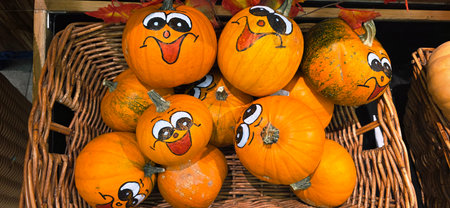 Colorful pumpkins with cheerful painted faces are arranged in a rustic basket, creating a festive...