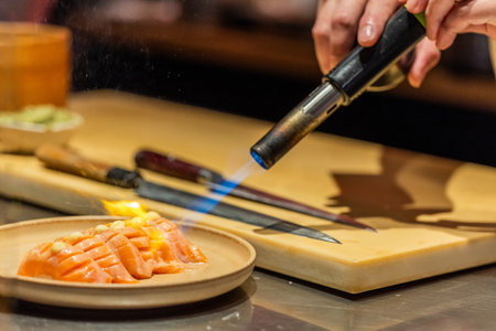 Chef is using a culinary torch to sear salmon fillet on a plate, showing skillful cooking techniques in a contemporary kitchen setting.の写真素材
