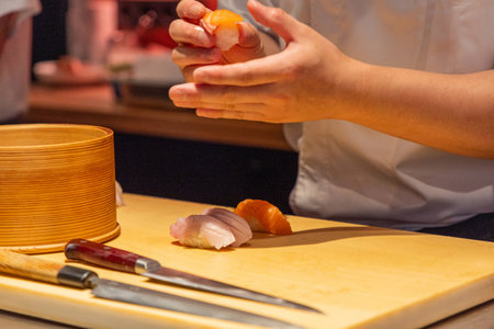 Sushi chef is skillfully preparing fresh sushi rolls on a wooden cutting board, showing culinary expertise and vibrant ingredients.の写真素材