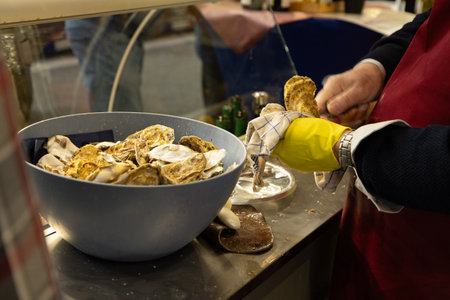 Seafood vendor is shucking fresh oysters in a vibrant market, showcasing culinary skills and fresh...