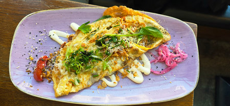 Gourmet omelette is beautifully plated with fresh herbs, sauces, and colorful garnishes, showcasing culinary artistry and presentation.の写真素材