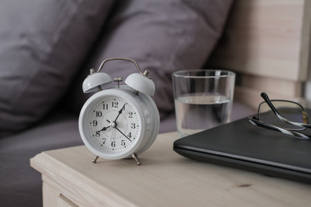 Alarm clock, laptop and glasses on the nightstand. Remote work in the comfort of your own home. Cozy...