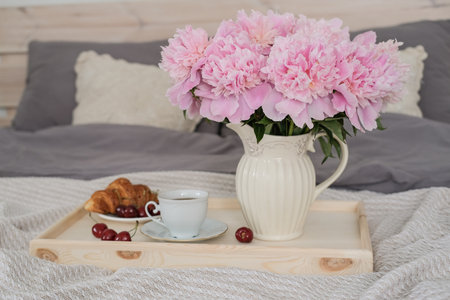Breakfast in bed. Tray with coffee, croissants and a bouquet of peonies on the bed in the bedroomの写真素材