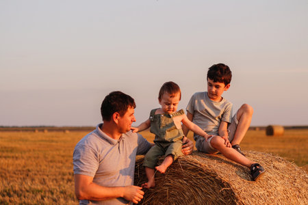 Dad with two sons in the field at sunset. Concept of friendly family and summer vacationの写真素材
