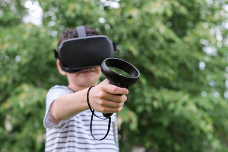 A seven-year-old boy in virtual reality glasses plays outside in the park. Children using technology. selective focusの写真素材