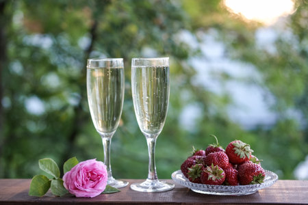 Glasses of champagne and strawberries on a terrace in a summer garden against the backdrop of evening sunlightの写真素材