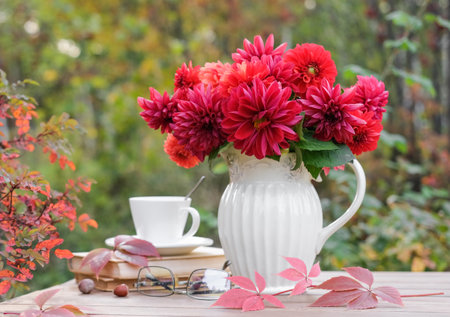 Vase with red autumn flowers and books on the table in the autumn garden. autumn still lifeの写真素材