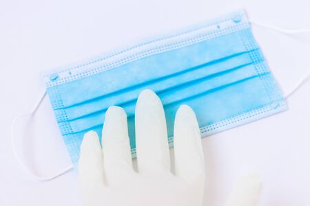 Medical white latex glove as a hand reaches for a blue mask on a white background. Concept. Remedies...