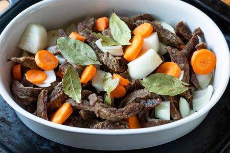 White dish with meat, carrots, onions and laurel on a black pan. の写真素材