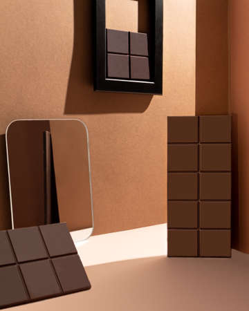 Mock-up three dark milk chocolate bars, geometry, lines, minimalism on a beige paper background. Reflection of chocolate in the mirror. Trending photo of chocolate. Chocolate in a black frameの写真素材