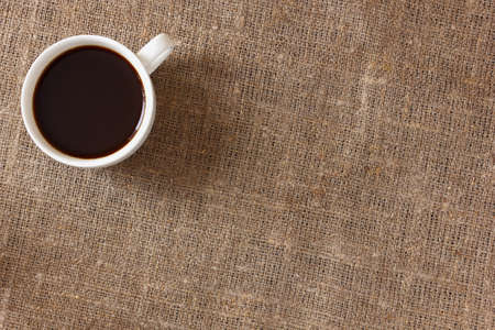 White mug with coffee on rough burlap tablecloth, top view.の写真素材