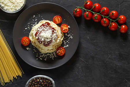 Pasta spaghetti Italian with parmesan and ingredients for cooking, tomatoes, spices, macaroni, grated cheese, top view dark background, with space to copy text.の写真素材