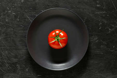 Tomato red one, on gray plate, top view dark background.の写真素材