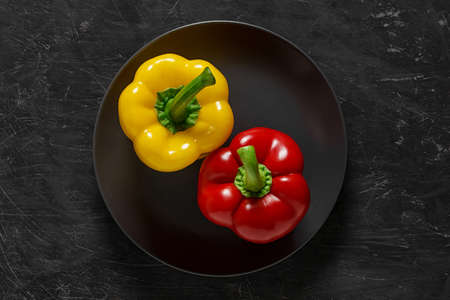 Peppers two bulgarian sweet yellow and red on gray plate top view dark background, with space to...