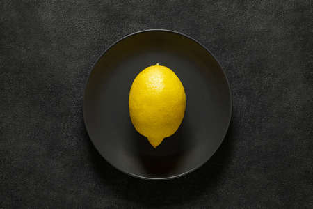 One whole lemon on grey plate, on dark background, top view, space to copy text.の写真素材