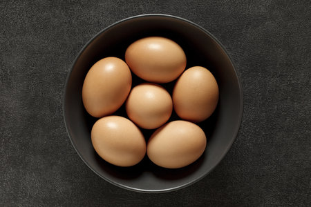 Eggs whole chicken in grey bowl, on dark background, top view, space to copy text.