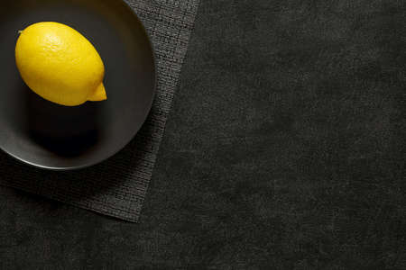 Lemon whole on gray plate, on dark background, top view, space to copy text.の写真素材