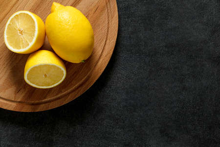 Lemons whole and cut on round wooden cutting board, on dark background, top view, space to copy text.の写真素材